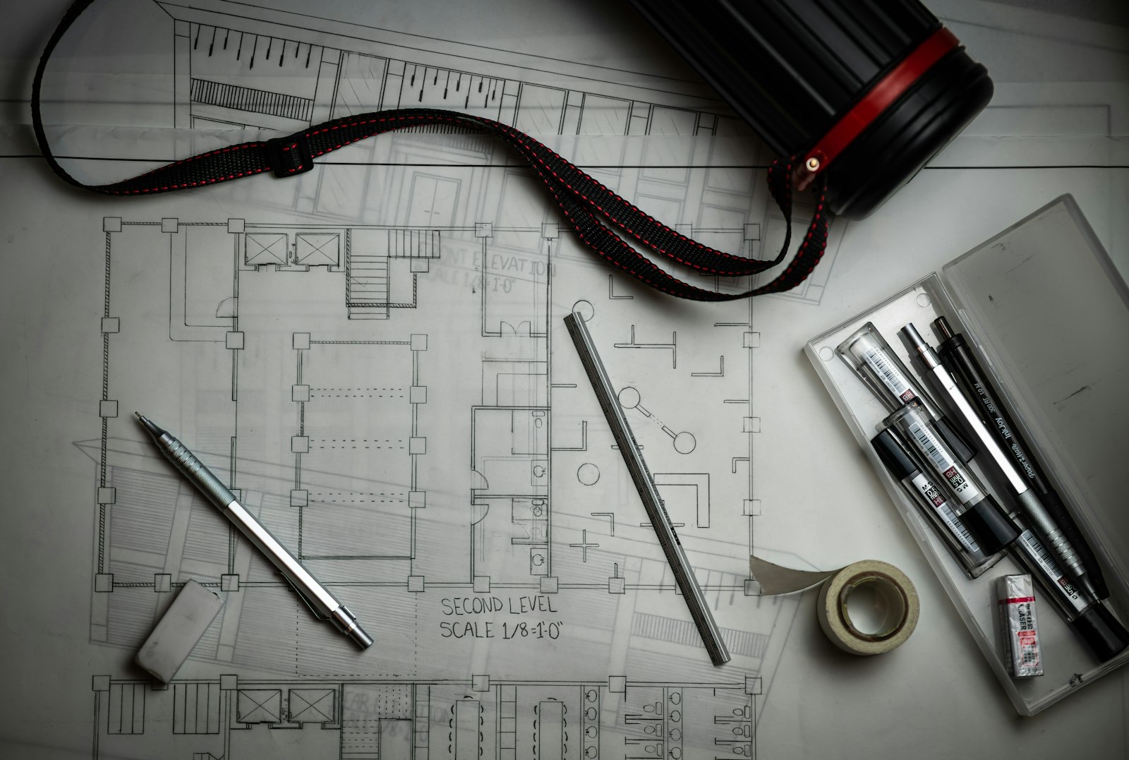 Plans techniques déroulés avec crayons de dessin, règle métallique et instruments de tracé.