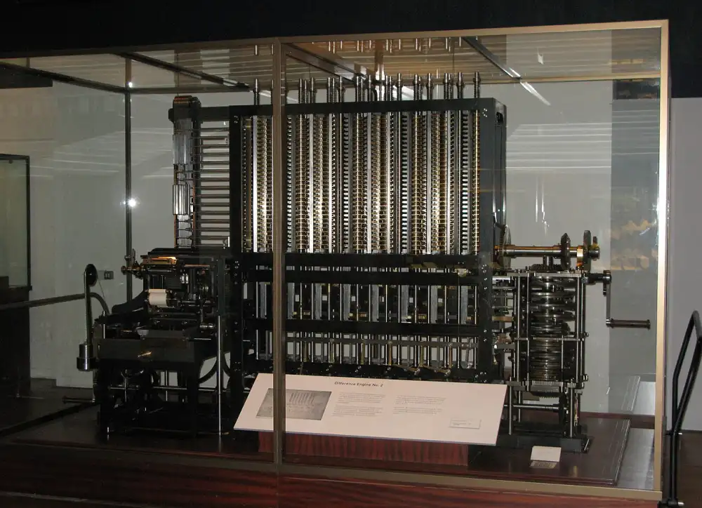 Machine à calculer mécanique en fonte et laiton, exposée sous vitrine. Des dizaines de colonnes verticales portent chacune une pile de roues dentées chiffrées ; à gauche, un mécanisme d&rsquo;impression, à droite, une manivelle et son train d&rsquo;engrenages.